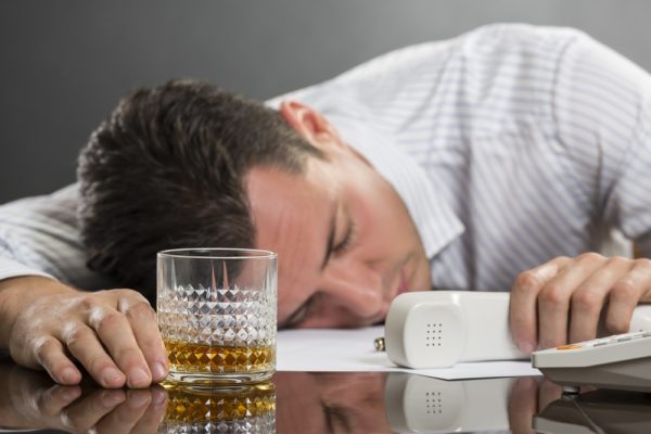 Мужчина с телефонной трубкой в руке и стаканом спит на столе